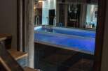 Step down into a luxurious indoor swimming pool area, complete with vibrant blue lighting and sleek chrome railings.