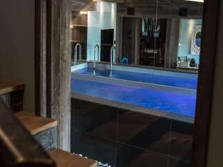Step down into a luxurious indoor swimming pool area, complete with vibrant blue lighting and sleek chrome railings.