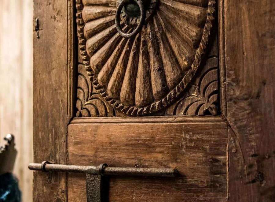 Step into a world of timeless elegance with this intricately carved wooden door, featuring a stunning sunburst motif and a rustic ring pull.