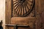 Step into a world of timeless elegance with this intricately carved wooden door, featuring a stunning sunburst motif and a rustic ring pull.
