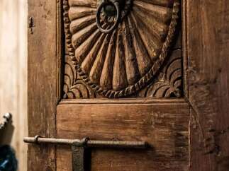 Step into a world of timeless elegance with this intricately carved wooden door, featuring a stunning sunburst motif and a rustic ring pull.