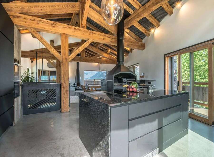 Experience luxury mountain living in this stunning open-plan kitchen and dining area, featuring exposed wooden beams and a modern fireplace.