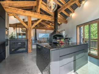Experience luxury mountain living in this stunning open-plan kitchen and dining area, featuring exposed wooden beams and a modern fireplace.