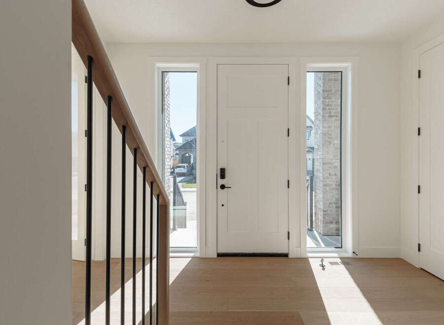Step into this bright and airy foyer, featuring a modern white door flanked by tall, narrow windows that flood the space with natural light.