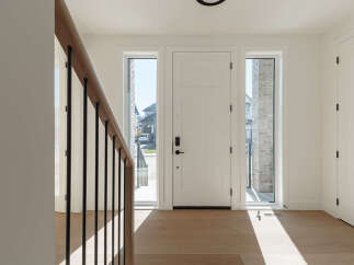 Step into this bright and airy foyer, featuring a modern white door flanked by tall, narrow windows that flood the space with natural light.