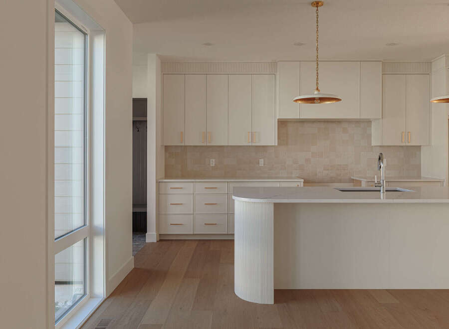 Experience modern luxury in this stunning kitchen, featuring sleek white cabinetry with elegant gold hardware and a chic tiled backsplash.