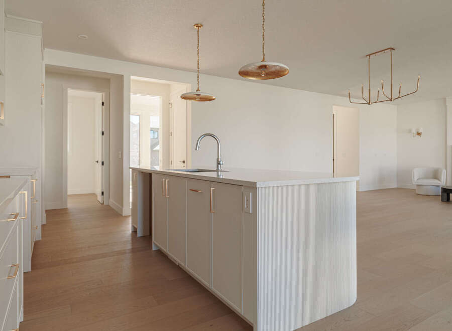 This modern kitchen boasts a sleek island with a waterfall countertop and a contemporary faucet, complemented by fluted cabinetry and brushed gold hardware.