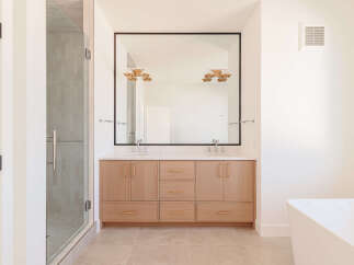 This modern bathroom features a spacious double vanity with light wood cabinetry and sleek rose gold hardware, complemented by a large frameless mirror.