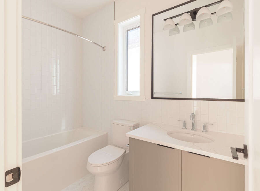 Step into this pristine bathroom, featuring a sleek bathtub with white tiled walls and a modern vanity with a quartz countertop.