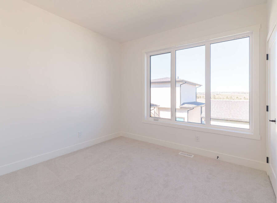 This empty room features a large window that floods the space with natural light, offering a view of neighboring houses and the surrounding landscape.