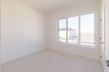 This empty room features a large window that floods the space with natural light, offering a view of neighboring houses and the surrounding landscape.