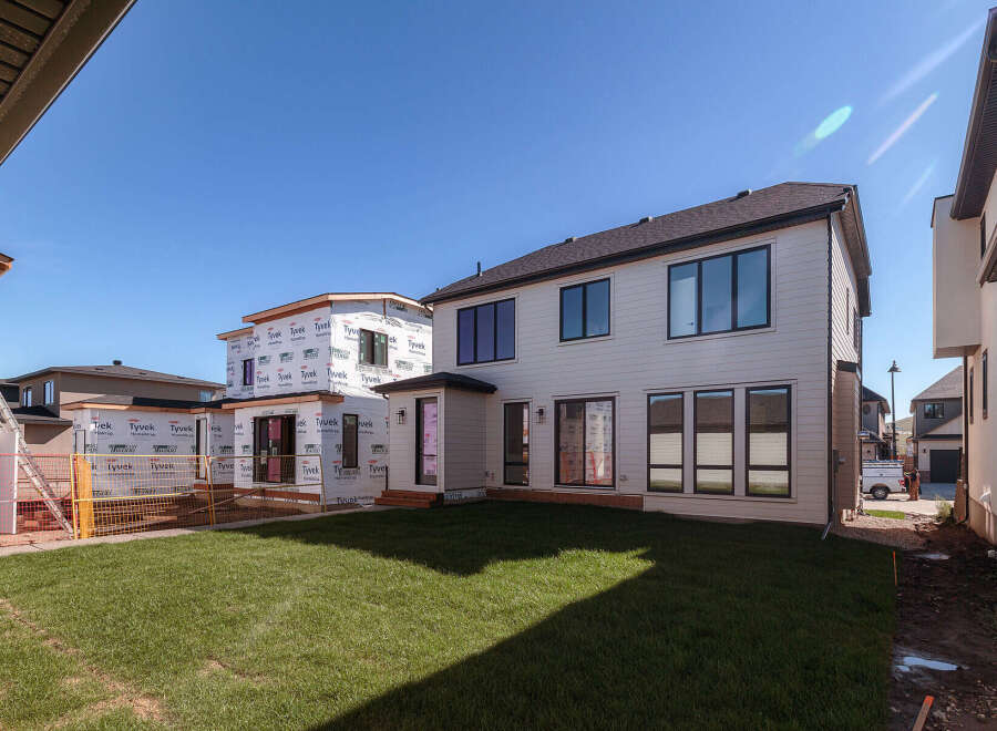 This image showcases a modern home under construction, featuring a sleek white exterior and large, dark-trimmed windows.