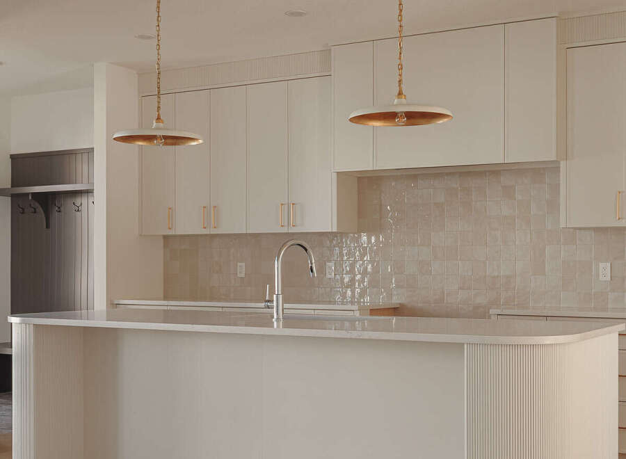 Experience modern luxury in this stunning kitchen, featuring sleek white cabinetry and a spacious island with a waterfall countertop.