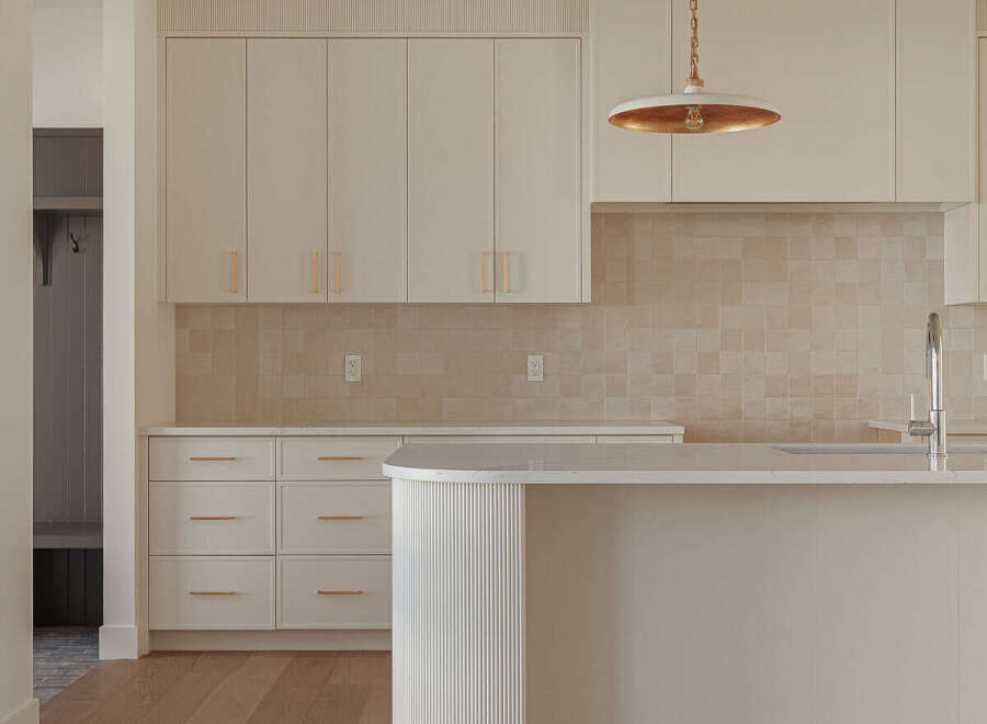 This modern kitchen boasts sleek, cream-colored cabinetry with subtle gold hardware, complemented by a warm, tiled backsplash.
