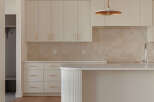 This modern kitchen boasts sleek, cream-colored cabinetry with subtle gold hardware, complemented by a warm, tiled backsplash.