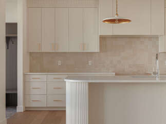 This modern kitchen boasts sleek, cream-colored cabinetry with subtle gold hardware, complemented by a warm, tiled backsplash.