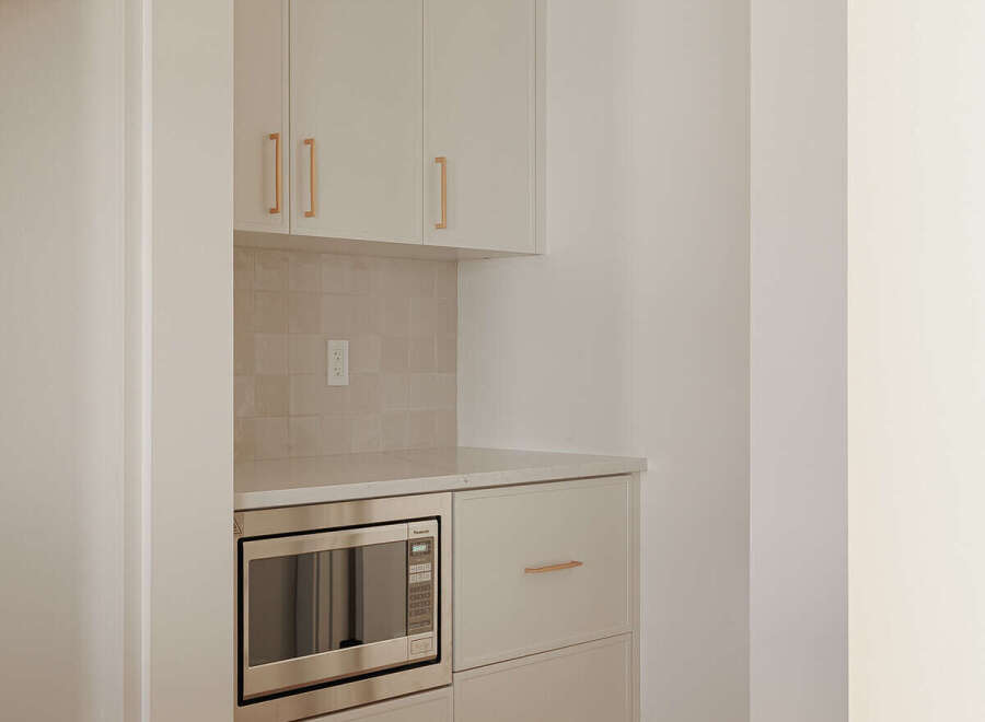 This modern kitchen features sleek, cream-colored cabinetry with elegant brass hardware, offering ample storage.