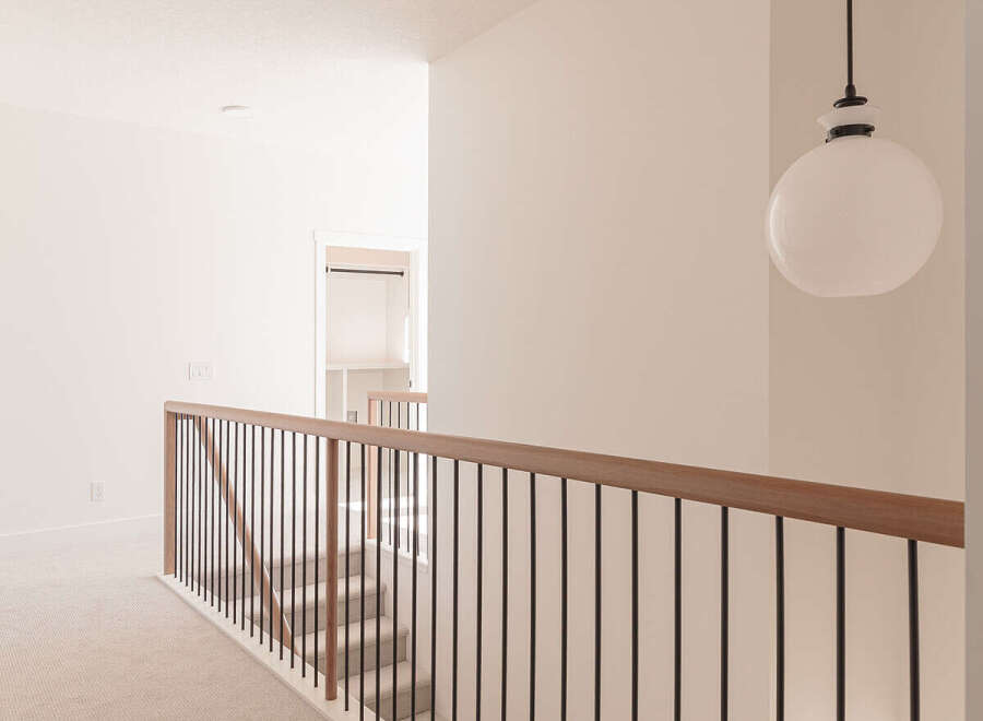 This modern hallway features a sleek black metal railing with a warm wood handrail, leading down a carpeted staircase.