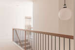 This modern hallway features a sleek black metal railing with a warm wood handrail, leading down a carpeted staircase.