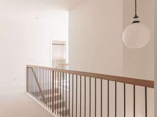 This modern hallway features a sleek black metal railing with a warm wood handrail, leading down a carpeted staircase.