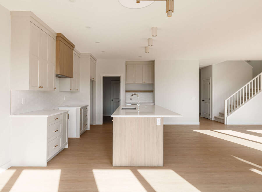 Experience modern living in this spacious open-concept kitchen, featuring sleek white cabinetry, a striking wood-accent island with a waterfall countertop, and a subway tile backsplash.