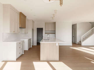 Experience modern living in this spacious open-concept kitchen, featuring sleek white cabinetry, a striking wood-accent island with a waterfall countertop, and a subway tile backsplash.