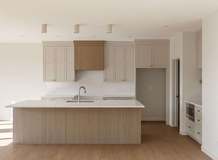 Experience modern living in this stunning kitchen, featuring sleek, light-colored cabinetry and a large island with a waterfall countertop.