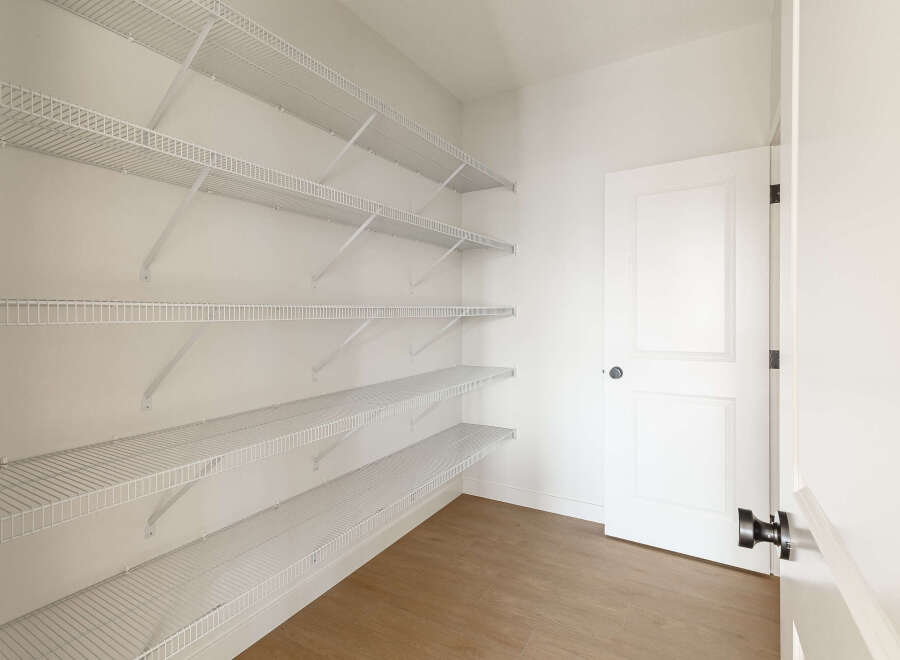 This spacious walk-in pantry offers ample storage with multiple rows of white wire shelving, perfect for organizing groceries and kitchen essentials.