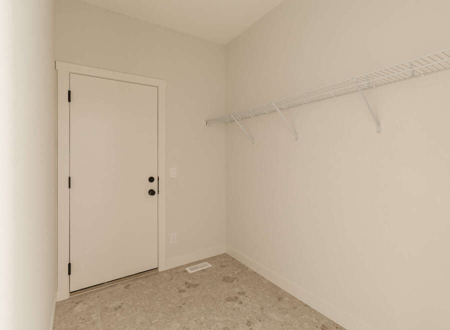 This empty room features a white door with black hardware, a white wire shelving unit mounted on the wall, and a floor with a marble-like tile pattern.