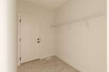 This empty room features a white door with black hardware, a white wire shelving unit mounted on the wall, and a floor with a marble-like tile pattern.