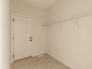 This empty room features a white door with black hardware, a white wire shelving unit mounted on the wall, and a floor with a marble-like tile pattern.