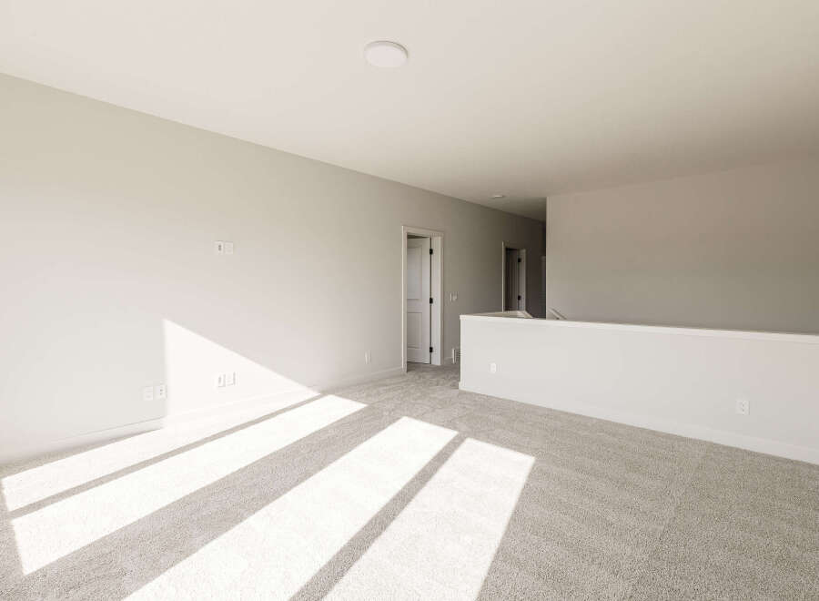 Sunlight streams across the plush carpet of this spacious loft area, highlighting the neutral tones and clean lines.