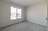This empty room features a large window offering a view of suburban homes and a plush, neutral-toned carpet.