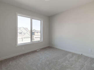This empty room features a large window offering a view of suburban homes and a plush, neutral-toned carpet.