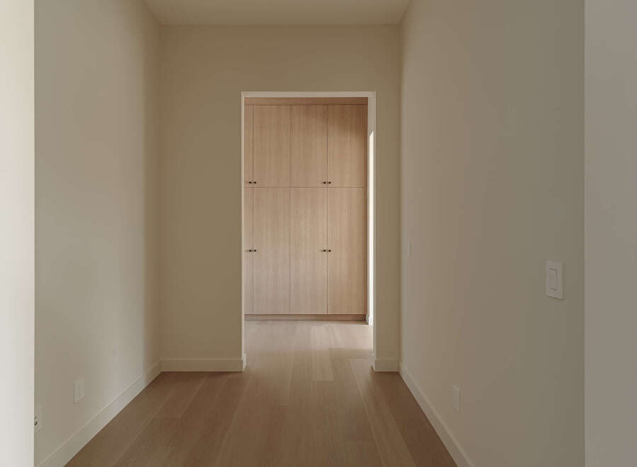 Step into this inviting hallway, featuring warm, light-toned hardwood floors that lead your eye towards a beautifully crafted built-in closet.