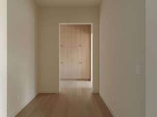 Step into this inviting hallway, featuring warm, light-toned hardwood floors that lead your eye towards a beautifully crafted built-in closet.
