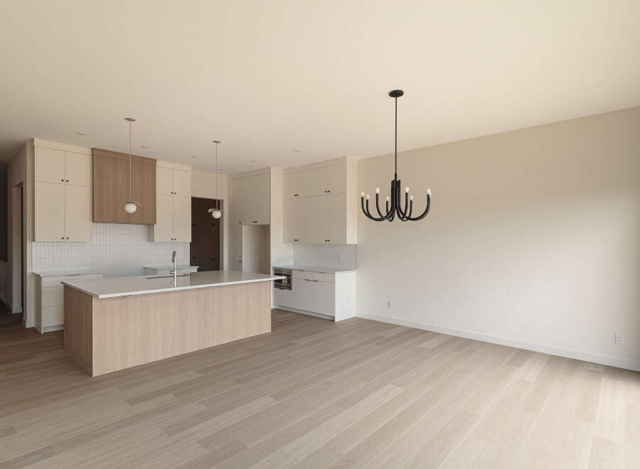 Experience modern living in this stunning kitchen and dining area, featuring sleek white cabinetry, a beautiful wood-accented island with a quartz countertop, and a striking black chandelier.