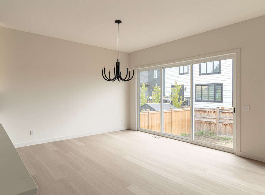 This modern dining area features a sleek black chandelier hanging above light wood flooring.