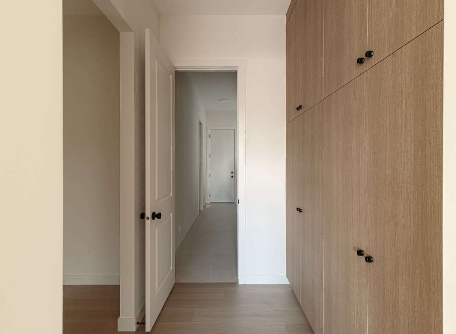 Step into a modern hallway featuring a sleek, light wood-paneled wall with minimalist black hardware, offering ample storage.