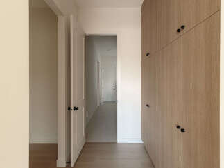 Step into a modern hallway featuring a sleek, light wood-paneled wall with minimalist black hardware, offering ample storage.