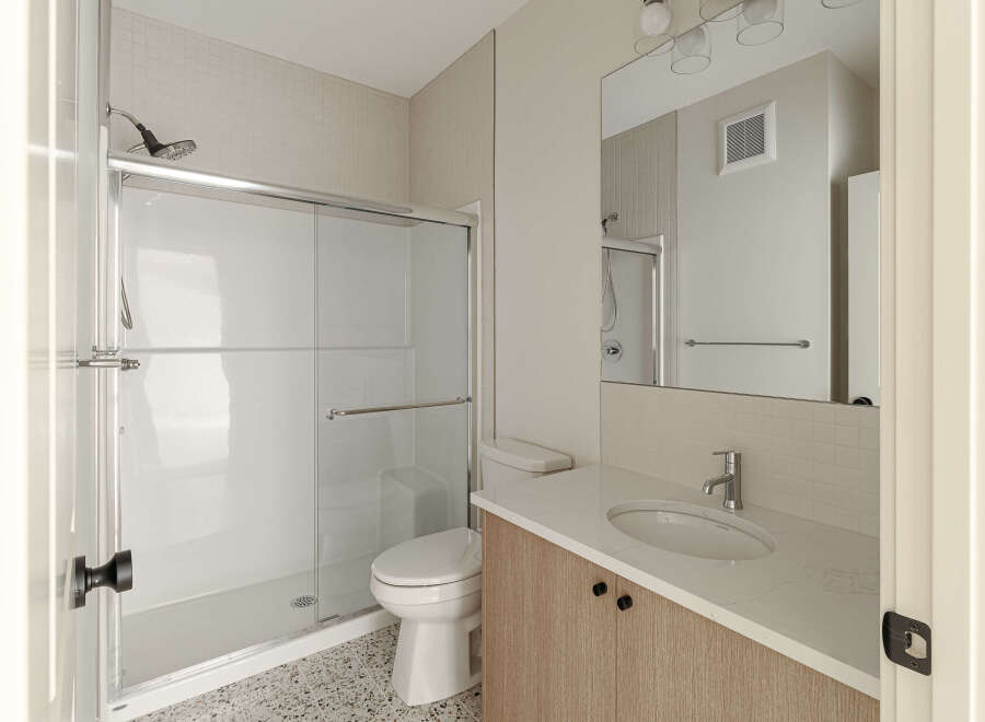 This modern bathroom features a sleek glass-enclosed shower with a chrome showerhead and a convenient handheld shower wand.