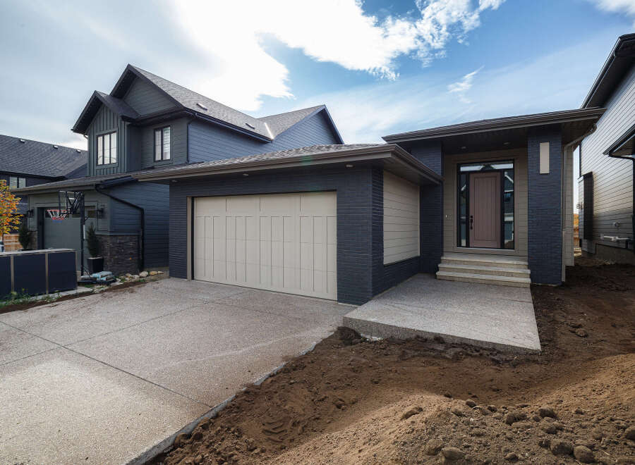 Discover modern living in this stunning dark-clad home featuring a sleek beige garage door and a welcoming entrance with stone steps.