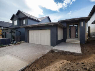 Discover modern living in this stunning dark-clad home featuring a sleek beige garage door and a welcoming entrance with stone steps.