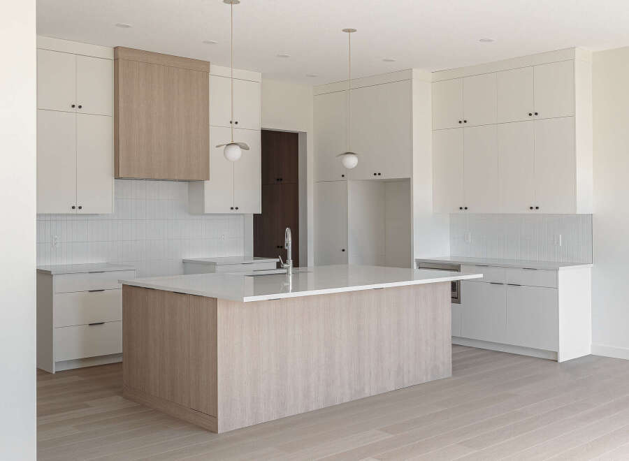 Experience modern luxury in this spacious kitchen, featuring sleek white cabinetry and a striking wood-paneled island with a waterfall countertop.