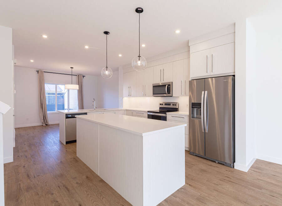 Experience modern living in this stunning kitchen, featuring sleek white cabinetry, a spacious island with a waterfall countertop, and stainless steel appliances.
