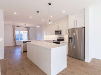 Experience modern living in this stunning kitchen, featuring sleek white cabinetry, a spacious island with a waterfall countertop, and stainless steel appliances.