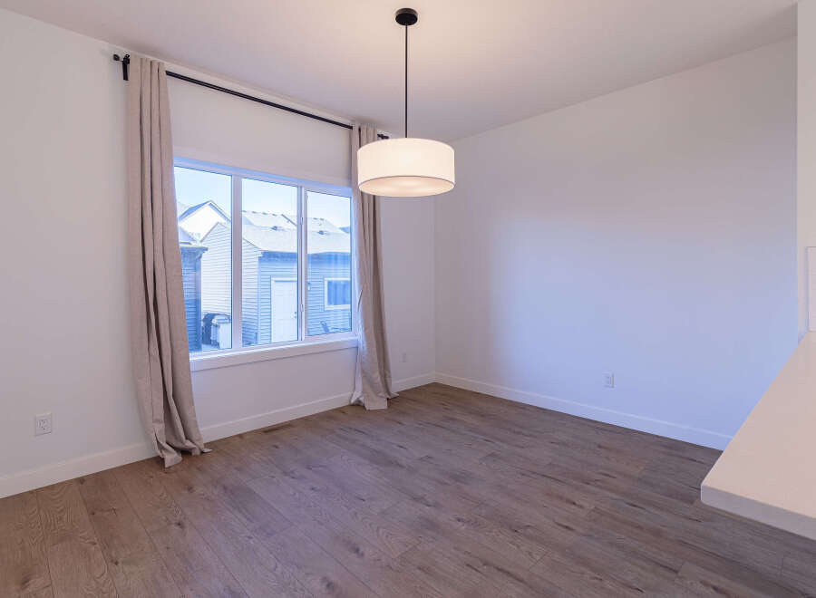 This dining area features a large window with neutral curtains, allowing natural light to flood the space.