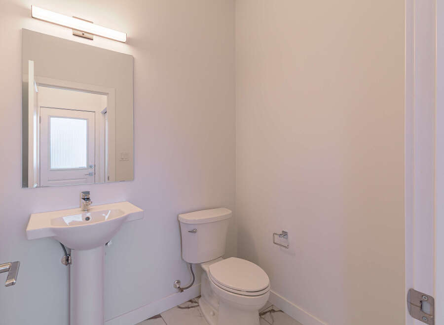 This modern bathroom features a sleek pedestal sink with a chrome faucet, complemented by a large mirror and a linear vanity light.