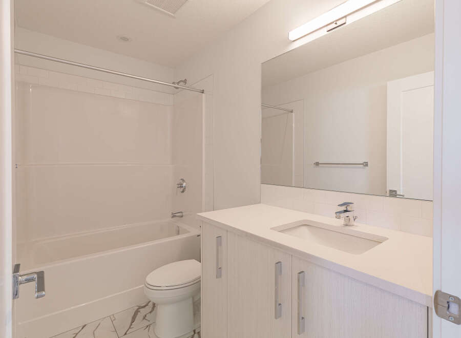 This modern bathroom features a pristine white bathtub and shower combination, complemented by sleek subway tile accents.