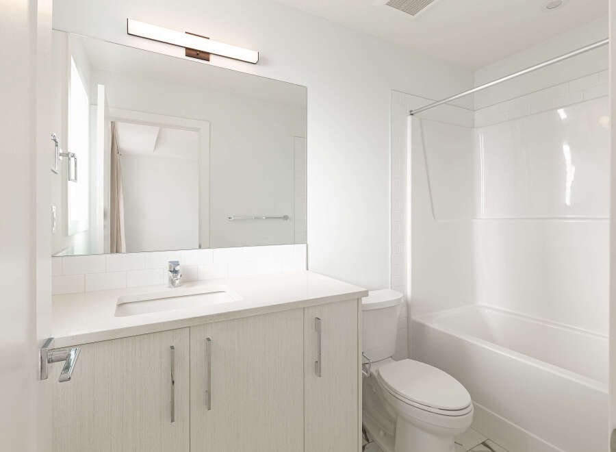 This modern bathroom features a sleek vanity with a white countertop and ample storage, complemented by a large mirror and a stylish vanity light.